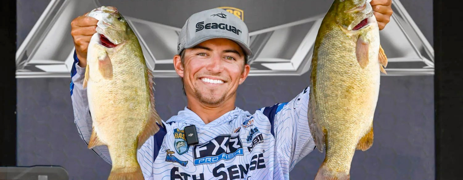 Photo of a smiling Trey McKinney holding two winning bass. His hat features sponsor Seaguar.