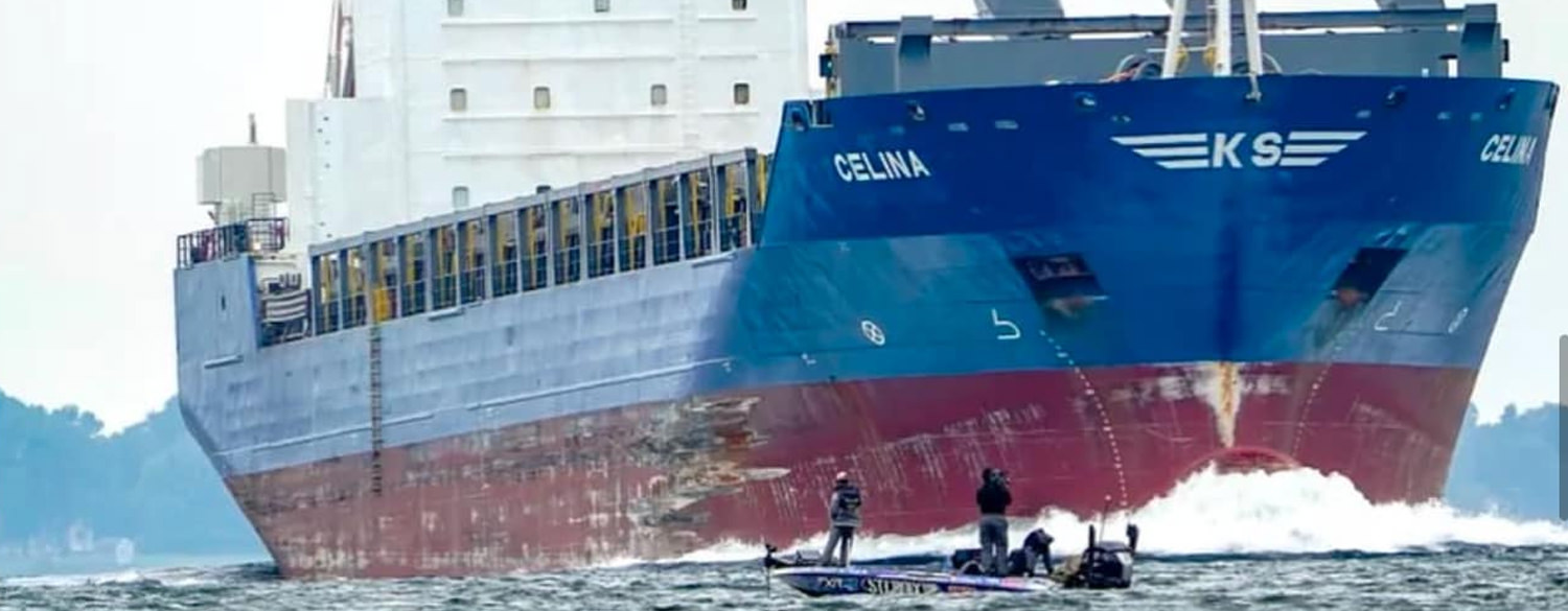 Photo of Trey McKinney in his bass boat beside an enormous cargo ship.
