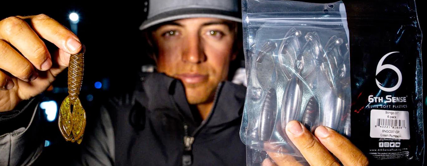 A nightime photo of Trey McKinney holding a Sixth Sense elite soft plastic lure and bag of metallic spinners.